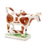 An early 19th Century cow creamer and cover with calf decorated with brown patches over the white