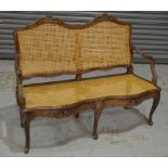 A late 19th to early 20th Century French bergere style two seat settee of serpentine outline,