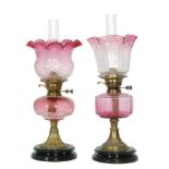 Two Victorian ruby oil lamps and shades each with conforming reservoirs on circular black glazed