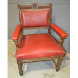 A Victorian oak elbow chair with central armorial back upholstered in red leather on turned legs