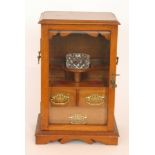 An early 20th Century twin handled, oak smoker's cabinet with three drawers behind a glazed door,