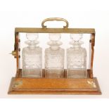A Victorian three divisioned oak tantalus with plated spirit labels and key, width 39cm.