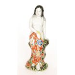 A Japanese figure of a scantily clad lady leaning against a tree stump holding a patterned robe to