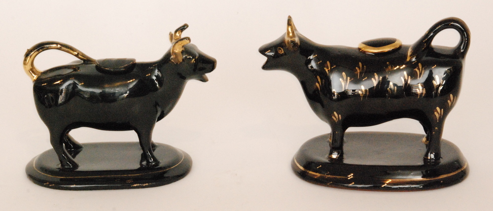 Two 19th Century Jackfield type cow creamers, each beast with gilt decoration on the black gloss