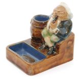 An early 20th Century Royal Doulton Lambeth vesta and ashtray formed as a seated man smoking a pipe