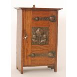An Art Nouveau oak smokers cabinet, the fitted pipe rack enclosed by a beaten copper panel door,