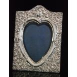 An Edwardian hallmarked silver heart shaped easel photograph frame with embossed foliate decoration