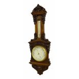 Walnut carved aneroid barometer/thermometer, the 8" silvered dial within an architectural foliate