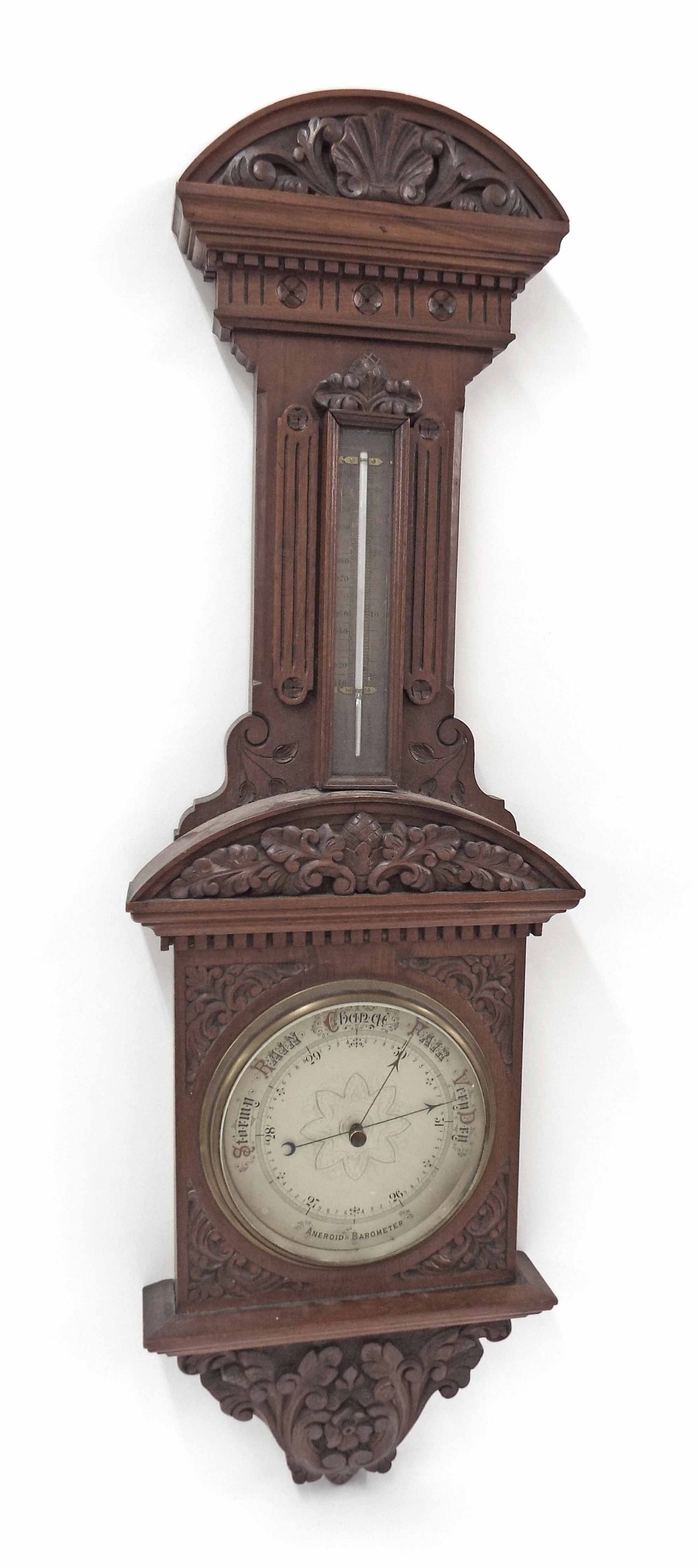 Mahogany aneroid barometer/thermometer, the 8" silvered dial within a foliate carved case surmounted