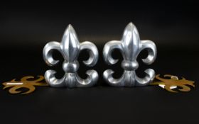 A Pair Of Modern Fire Dogs In white metal and gold tone Fleur De Lys Design.