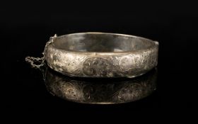 A Silver Hinged Bangle With Attached Safety Chain The front engraved with foliate decoration,