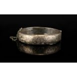 A Silver Hinged Bangle With Attached Safety Chain The front engraved with foliate decoration,