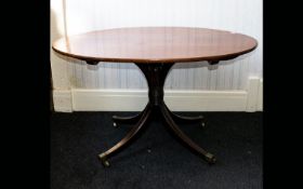 Edwardian tilt top table raised on quatrefoil base with brass castors. Oval top with warm, ages,