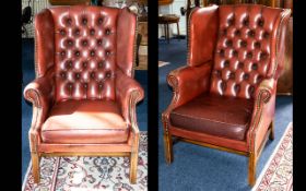 A Pair of Leather Club Chairs. Two wing-backed armchairs with traditional button back detail