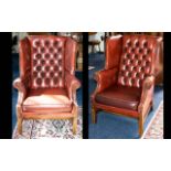 A Pair of Leather Club Chairs. Two wing-backed armchairs with traditional button back detail