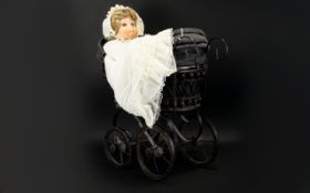 A Miniature Pram And Doll Victorian style pram in black metal with black canvas lining,