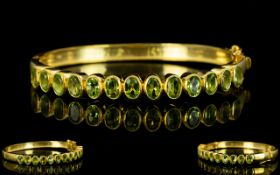 Peridot Hinged Bangle, a row of oval cut peridots totalling 6cts, bezel set, vertically,