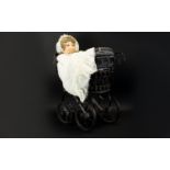 A Miniature Pram And Doll Victorian style pram in black metal with black canvas lining, together