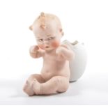 A German Heubach bisque piano baby, sitting upright with a cracked egg on its back, 13cm high.