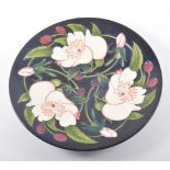 A Moorcroft shallow dish designed by N Slaney, navy blue ground with white flowers and berries,