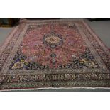 A Meshed carpet, central floral medallion against a burgundy ground with scrolling palmette design,