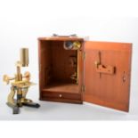 A mahogany cased brass microscope, with eye piece and objectives on cast black metal stand,