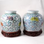 Pair of Chinese jars, of shouldered form, flat lids, floral decoration in colours, on stands, 30cms.