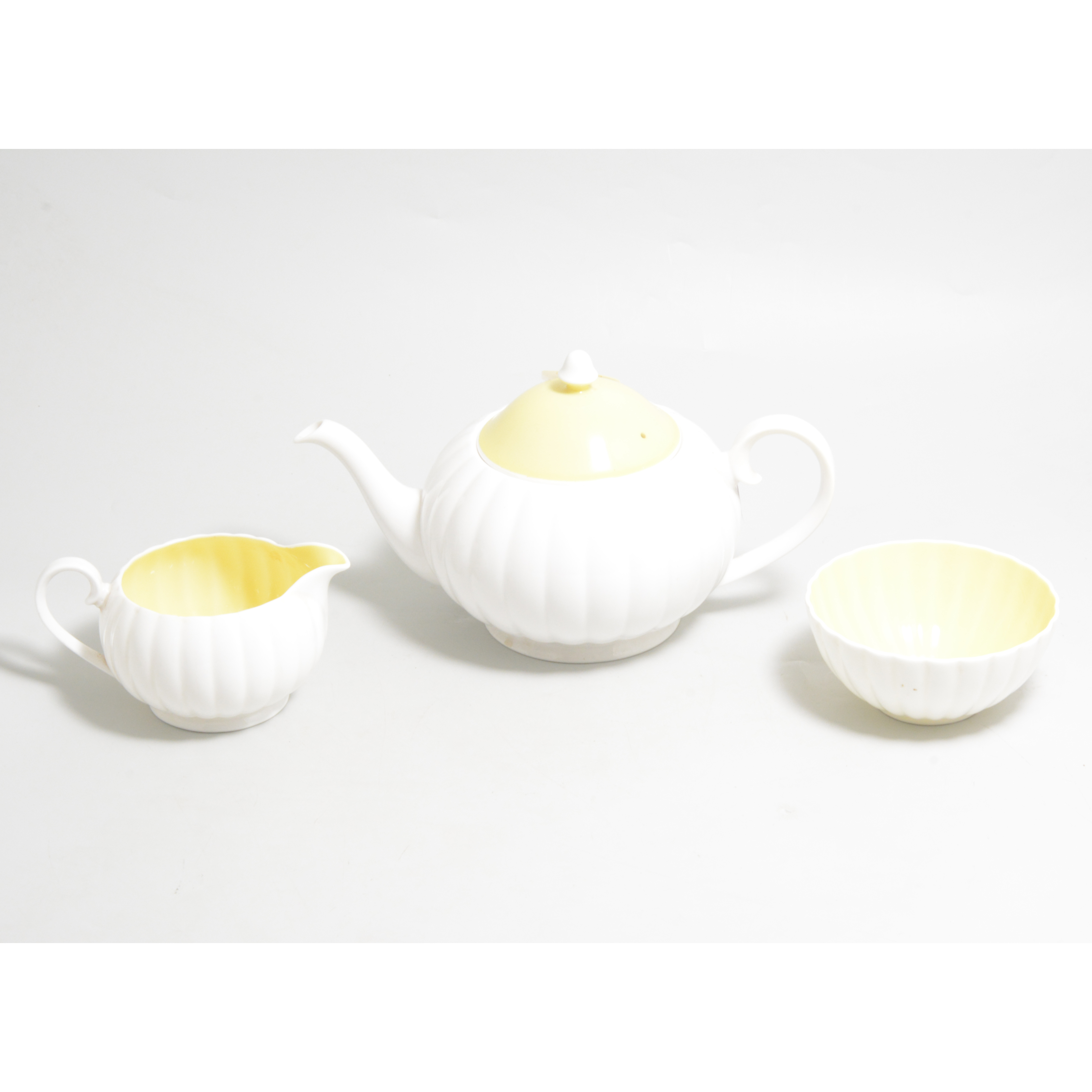 A Susie Cooper three piece teaset, white flute design with yellow interior and cover to teapot.