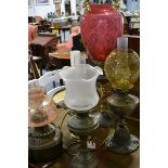 Six oil lamps, brass and chrome-plated, one having a large cranberry glass shade, all with chimneys,