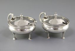 A pair of George V Arts & Crafts silver mustard pots with matching spoons, by Albert Edward Jones,