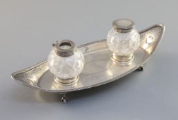 A George III silver boat shaped inkstand, with two silver mounted glass bottles, on an engraved base