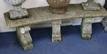 A weathered composition garden bench, of concave rectangular form, with three scroll plinths, 4ft