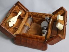 An early 20th century Harrod's crocodile skin toilet case containing four silver mounted toilet