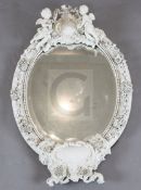 A late 19th century German porcelain wall mirror, of oval form with twin cherub and crown crest