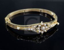 A late Victorian high carat gold, diamond and seed pearl set hinged bangle, of pierced flower head