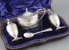 A cased late Victorian engraved silver three piece condiment set and spoon by Josiah Williams &