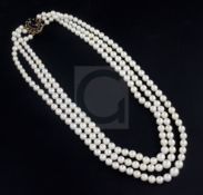 A triple strand graduated cultured pearl necklace with garnet cluster set oval gold clasp, 60cm.
