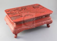 A Chinese red lacquer low table, carved in relief with peacocks and pine to the top and flowers to