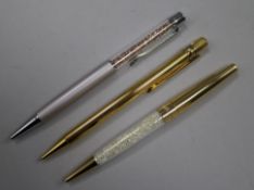 A Must de Cartier gilt ballpoint pen and two Swarovski ballpoint pens.From the estate of the late