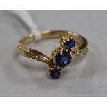 An 18ct gold and three stone sapphire crossover ring with diamond set shoulders, size L.