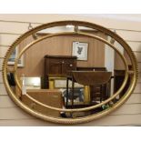 A gilt-framed oval wall mirror with marginal plates W.122cm