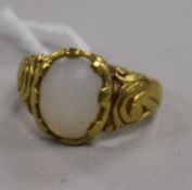 A yellow metal and moonstone? cabochon ring, the oval stone set on scrolled mount and shoulders (