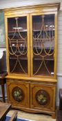 A Sheraton style painted and decorated satinwood bookcase cupboard W.112cm