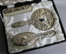 A cased modern three piece repousse silver mirror and brush set, Birmingham, 1977
