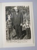 A black and white photograph of Albert Schweitzer standing with two children, apparently dated