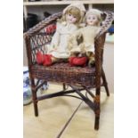 Two bisque headed 19th century dolls on a wicker chair