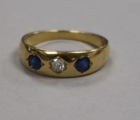 A yellow metal and three stone gypsy set sapphire and diamond ring, size O.