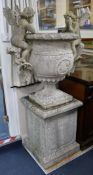 A garden urn, with cherub and goat's head mounts, on square plinth, H 165cm W.