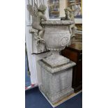 A garden urn, with cherub and goat's head mounts, on square plinth, H 165cm W.