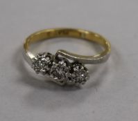 A yellow metal, platinum and illusion set three stone diamond crossover ring, size L.